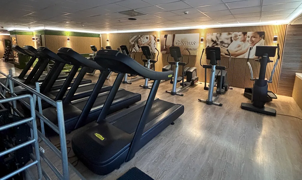 Futópadok és elliptikus trénerek sora a fa borítású kardiógalérián, a falon Corpus Fitness plakátok